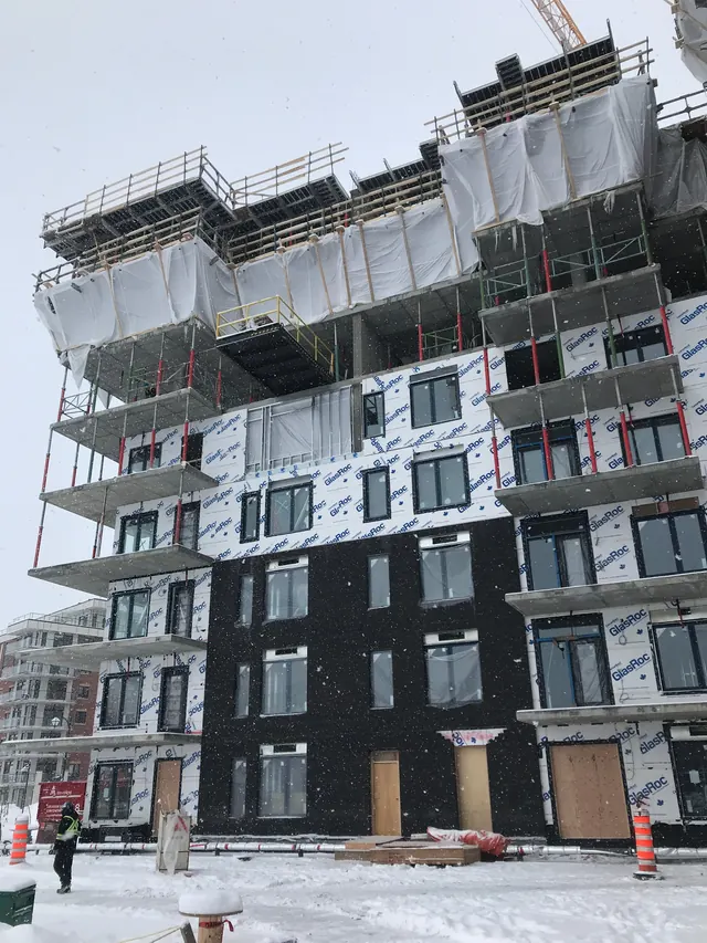 A mid-rise in winter: cladding on the lower floors, sheathing above, the frame still going up