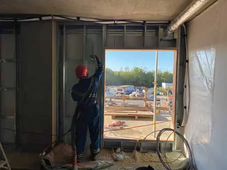 An installer spraying foam on an exterior wall from inside the building