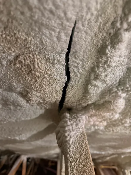Thick closed-cell spray foam on a roof deck with a long open crack where it meets a foam-covered rafter