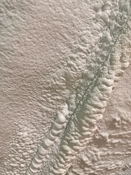 Rough closed-cell spray foam surface with a lumpy ridge where spray passes overlap