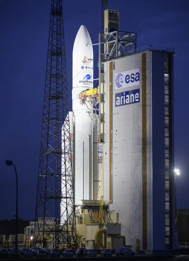 Europe’s white Ariane 5 rocket at night beside its launch tower in French Guiana