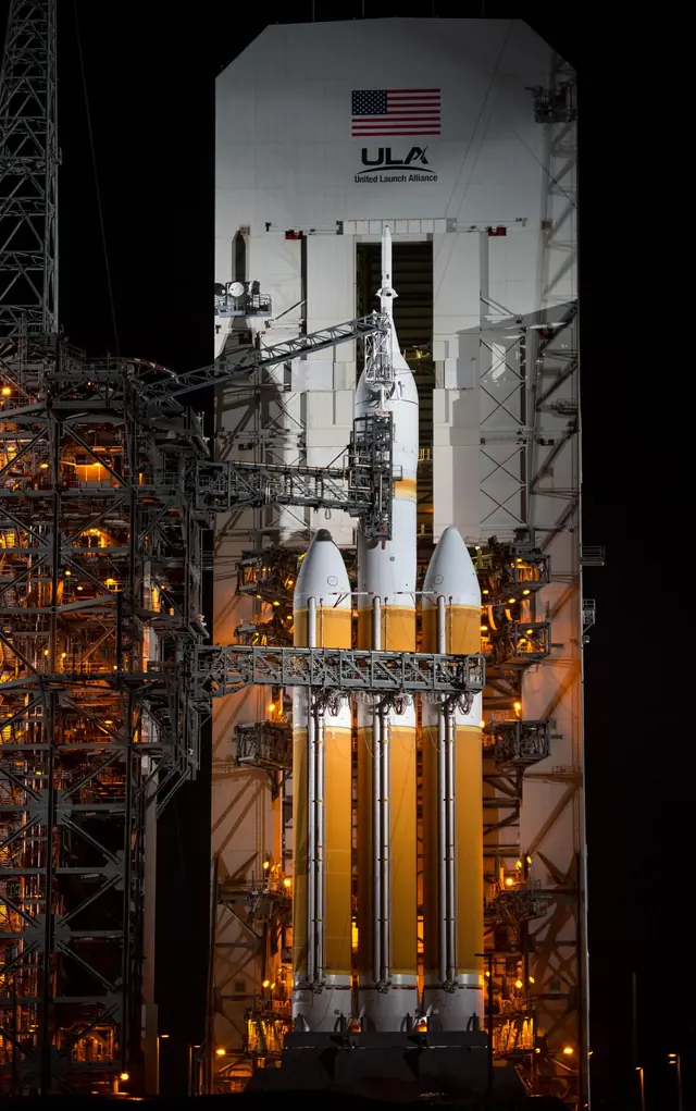 Delta IV Heavy at night on its launch pad: three orange booster cores side by side under a white upper stage