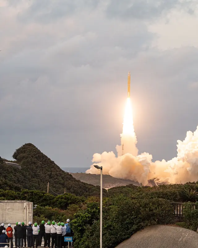 Japan’s H3 rocket climbing on a white plume from the coast of Tanegashima, spectators watching below