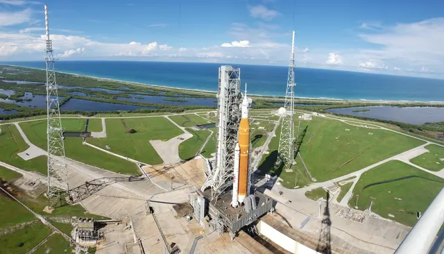 NASA’s Space Launch System on Launch Pad 39B, its tall orange core stage between two white boosters, with the Atlantic coast behind